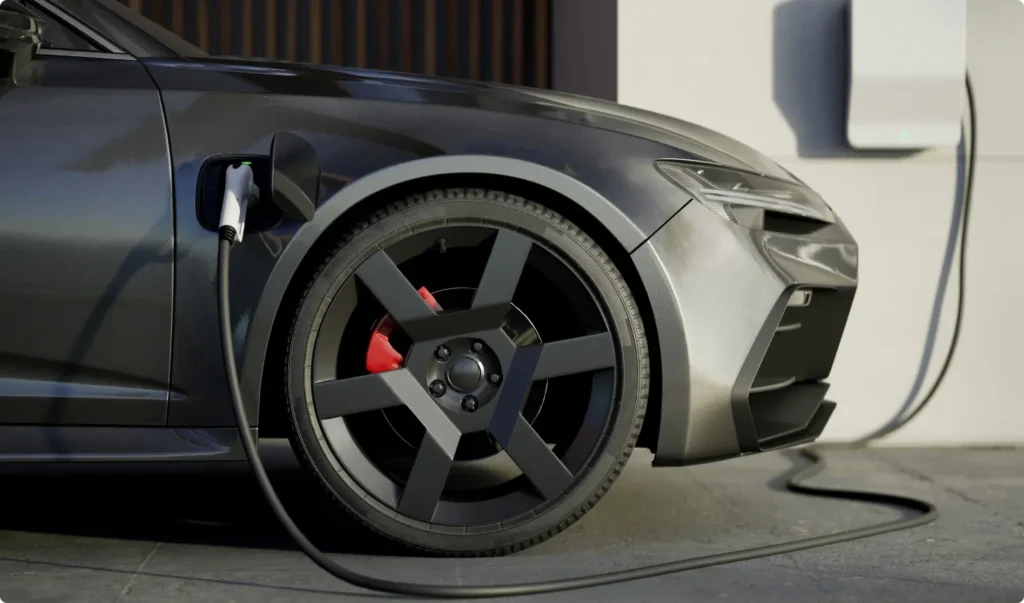 Close-up of a sleek electric car charging at a wall-mounted station, showing the front wheel, charging cable, and part of the cars metallic gray body.