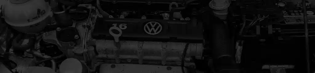 Close-up view of a Volkswagen car engine, highlighting the VW logo and 16 on the engine cover, with various engine components and parts visible around it.