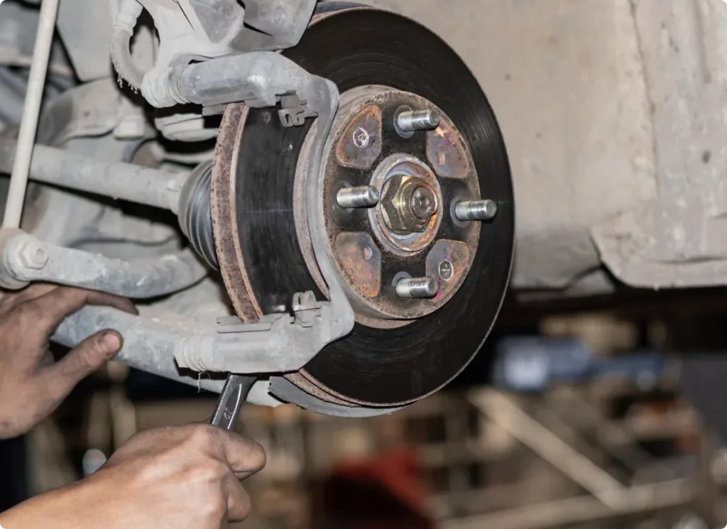 brake repair, auto repair in West Point, VA at Eltham Auto Clinic. A close-up of a mechanic’s hands working on a car’s exposed brake disc and caliper, using a wrench to make repairs or adjustments to the vehicle’s braking system.