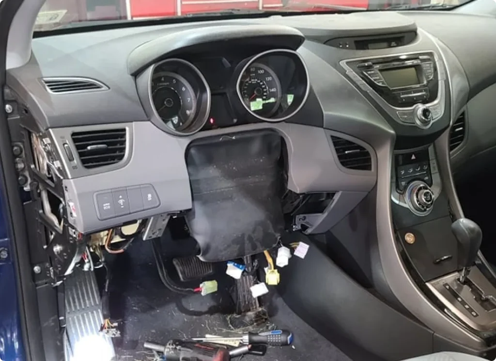 suspension repair, auto repair in West Point, VA at Eltham Auto Clinic. A car dashboard with the steering wheel removed, exposing wires and internal components. Car tools and parts are scattered on the floor near the pedals.