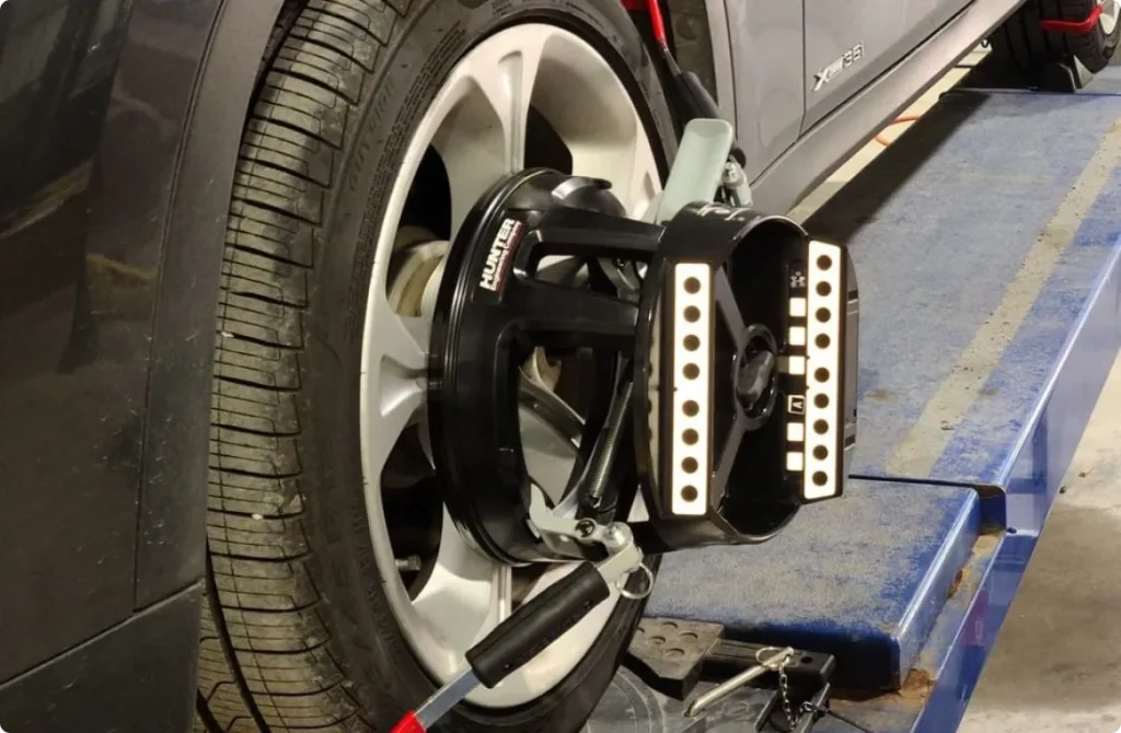 A car wheel with a Hunter alignment tool attached to the rim, set up on a workshop lift for wheel alignment service.
