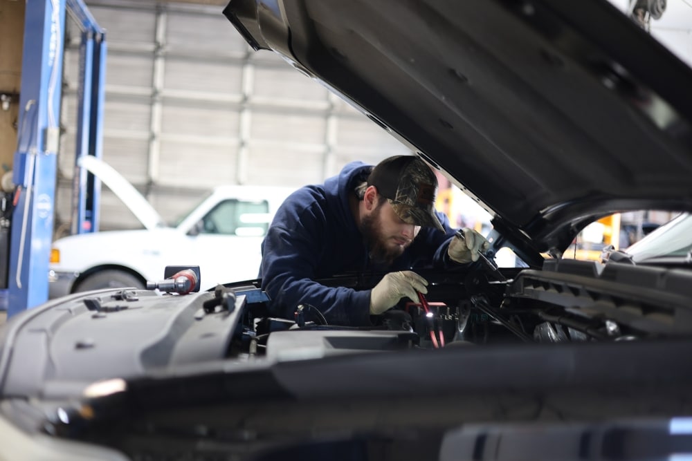 A mechanic inspecting under the hood of a car in a garage, performing a Virginia state inspection, Virginia State Inspection In West Point, VA At Eltham Auto Clinic